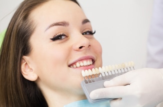 Dentist comparing custom dental veneers to smiling woman's teeth