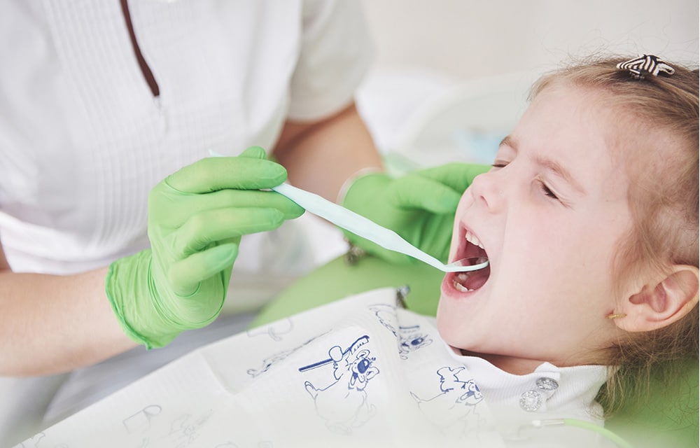 Friendly pediatric dentist inspecting scared child's teeth with dental mirror